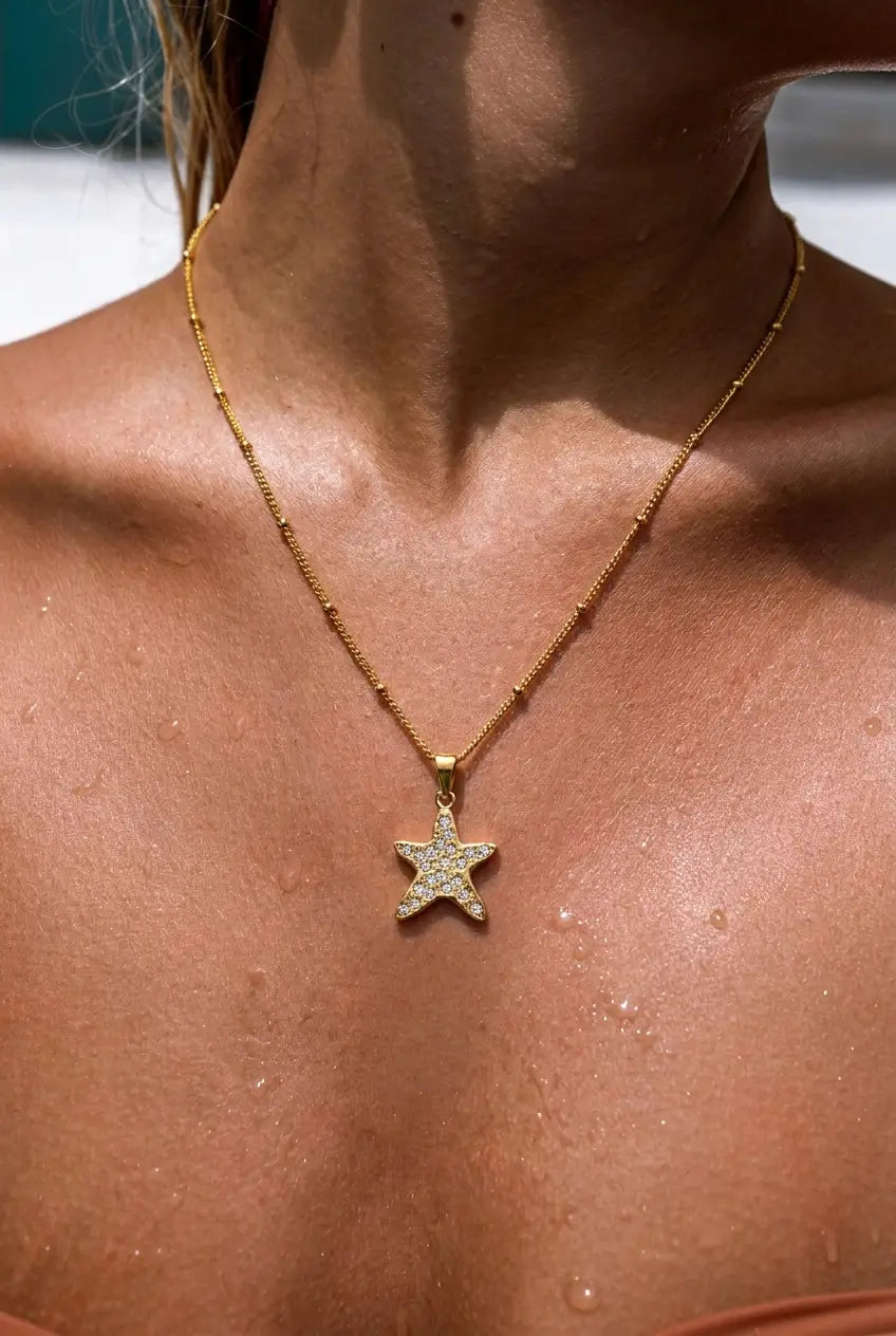 A close-up of a model's neck and chest wearing a delicate gold chain necklace with a starfish-shaped pendant studded with small clear crystals.