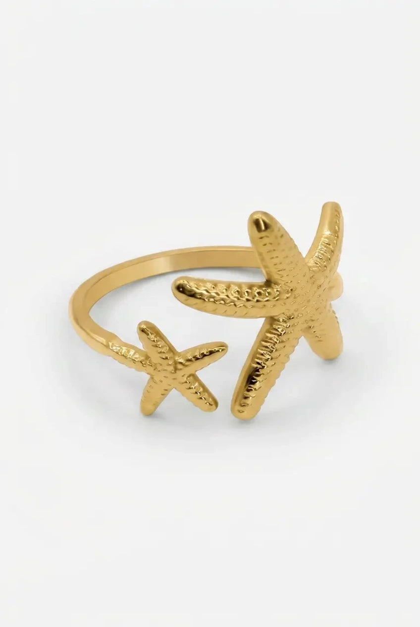 A gold-toned metal ring featuring two textured starfish designs, photographed on a clean white background.