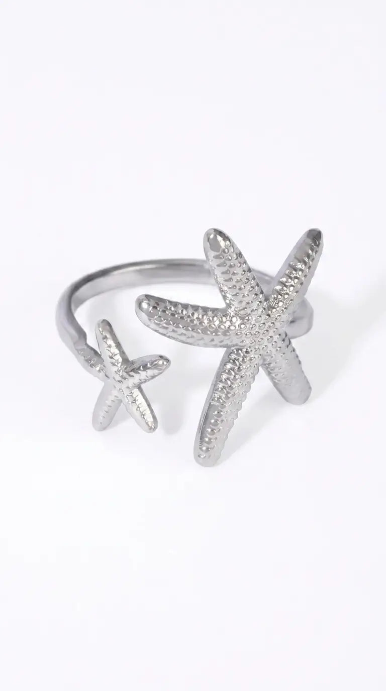 A silver-toned open ring featuring two textured starfish charms, one larger and one smaller, set against a plain white background.