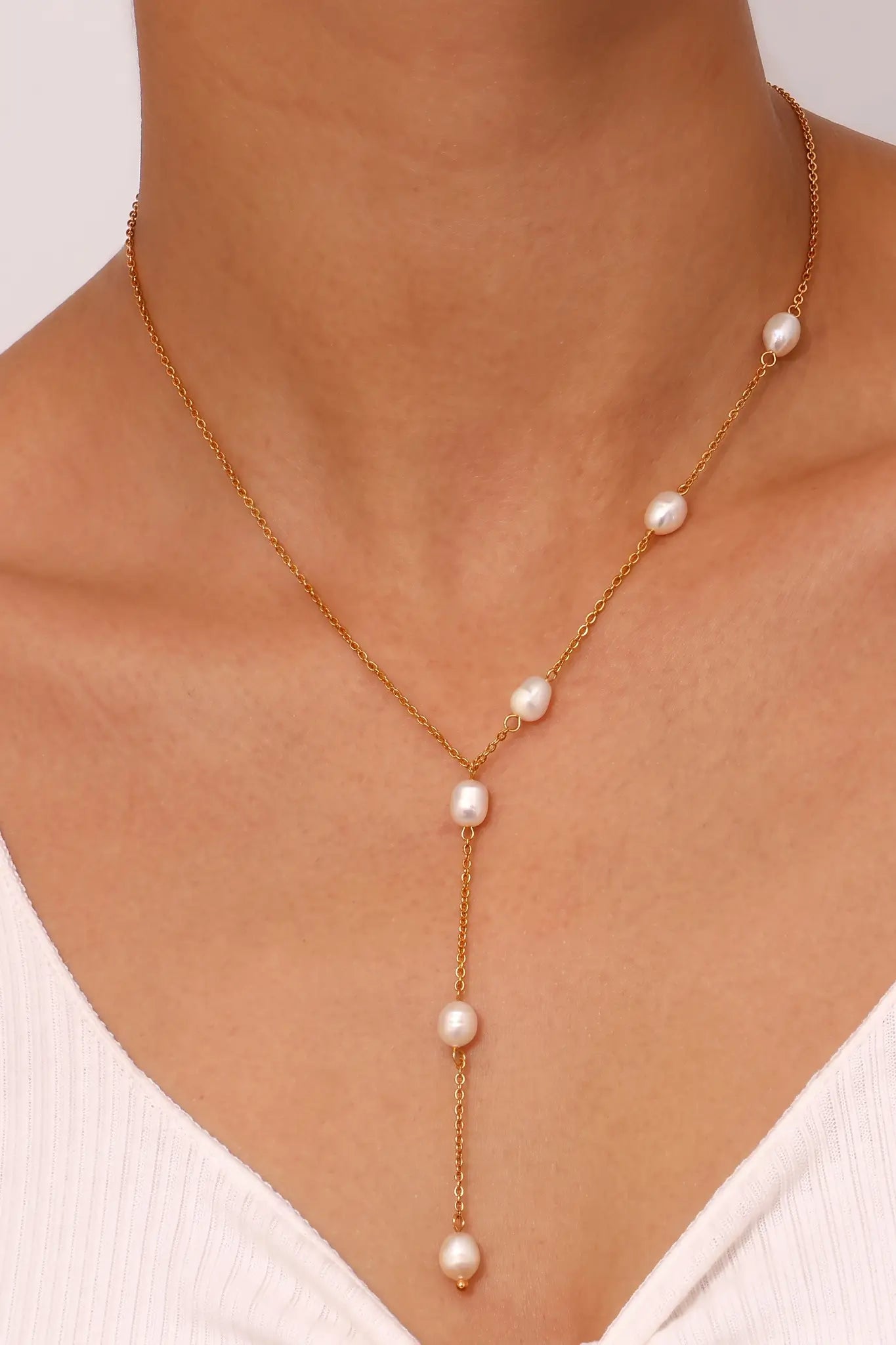 A gold Y-necklace with five white freshwater pearls, shown worn on a model's neck over a white ribbed top.