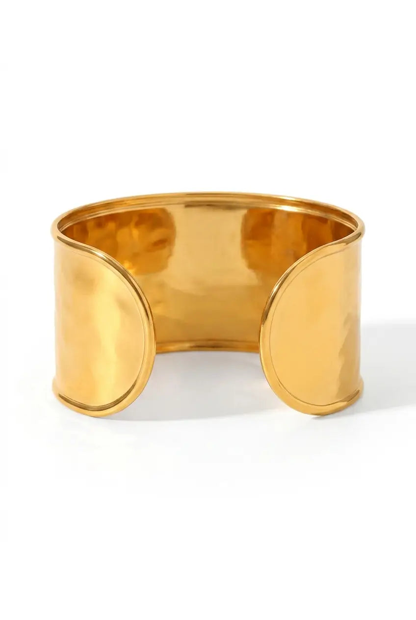 A wide, polished gold-tone metal cuff bracelet with a smooth, reflective surface, displayed on a clean white background.