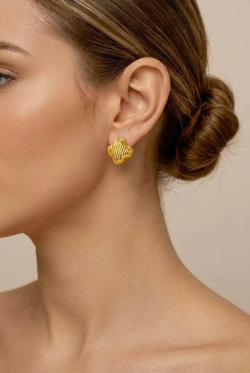 A close-up of a woman's ear and side profile wearing a textured gold stud earring against a soft beige background.
