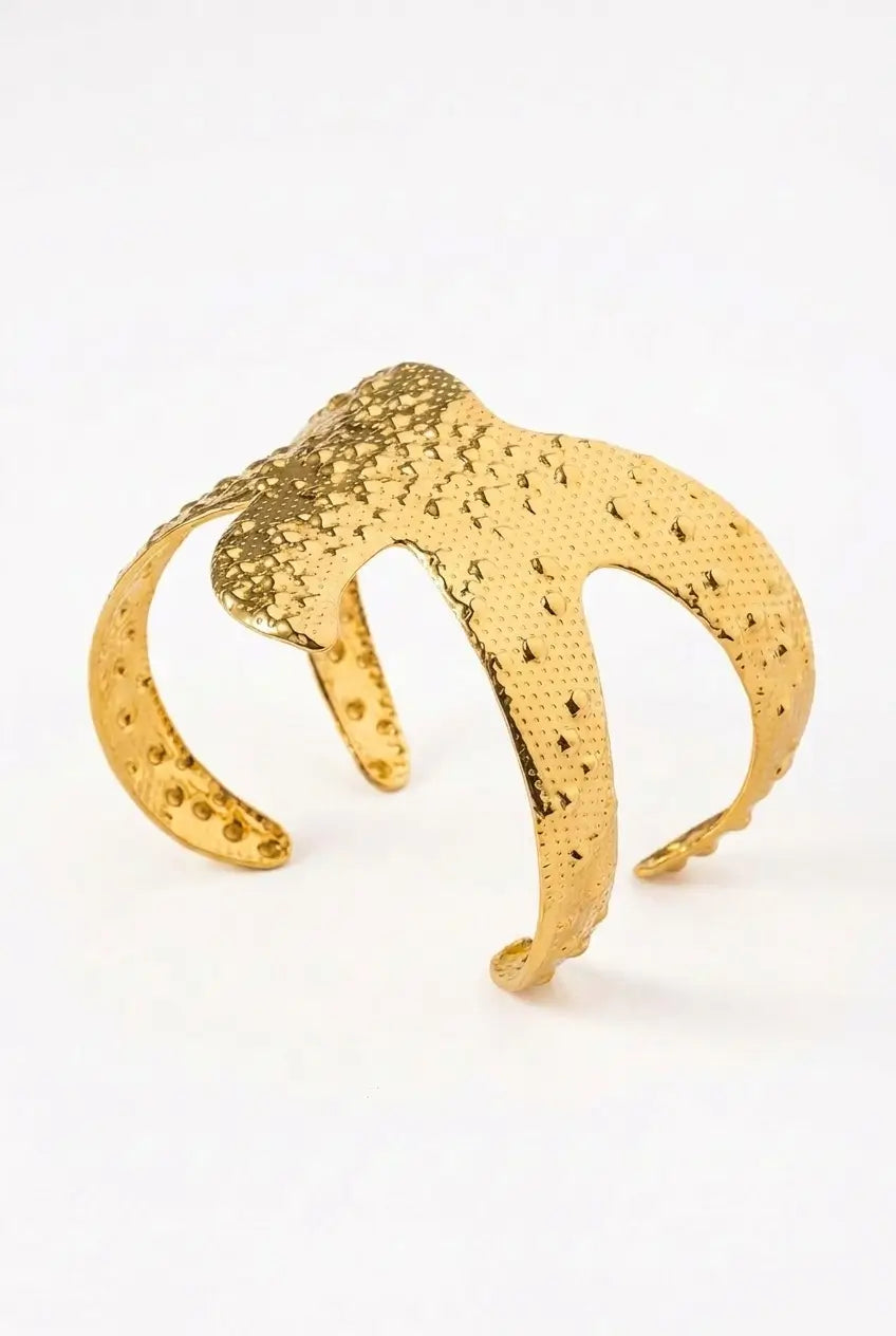 A textured gold-tone cuff bracelet with a honeycomb pattern and small raised dots, photographed on a clean white background.