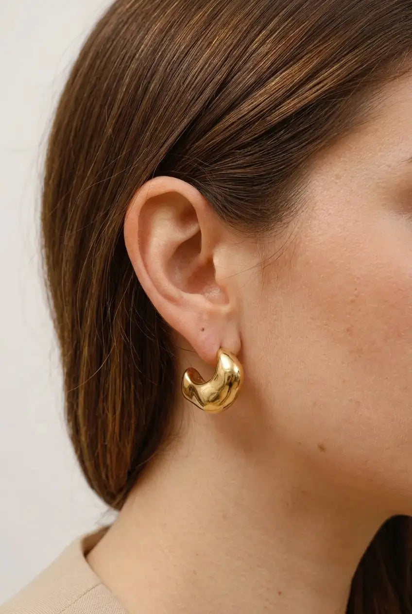 A close-up side profile of a woman wearing a chunky, organic-shaped gold hoop earring.