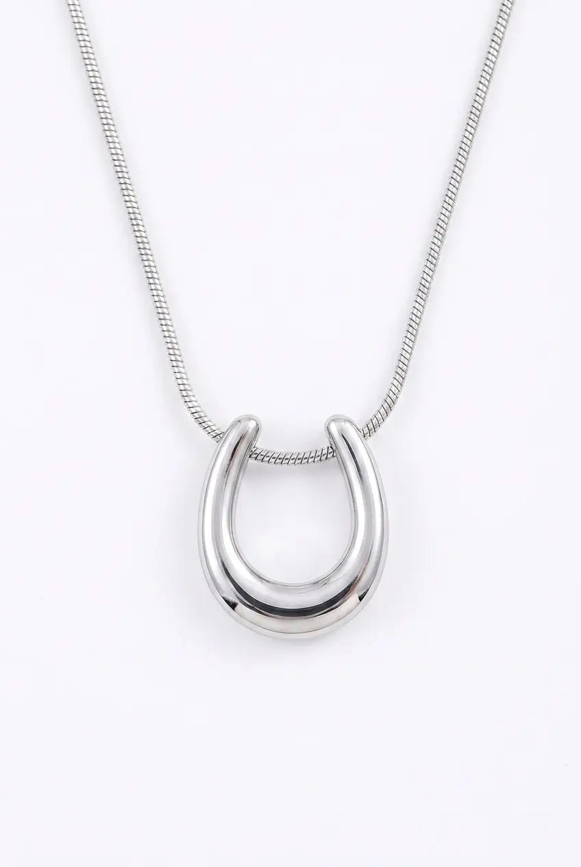 A polished silver horseshoe pendant necklace on a delicate silver snake chain, shown against a plain white background.