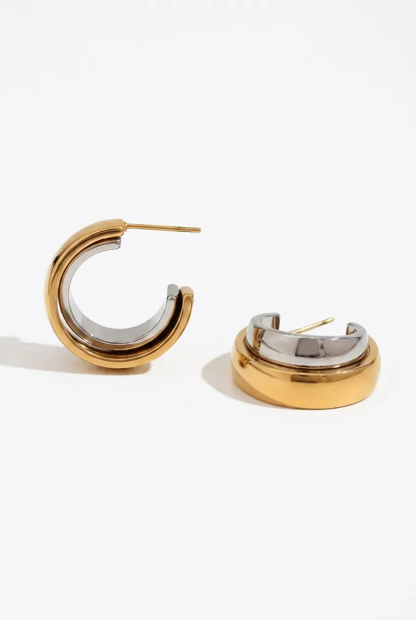 A pair of gold and silver two-tone hoop earrings shown on a clean white background, with one earring standing upright and the other lying on its side.