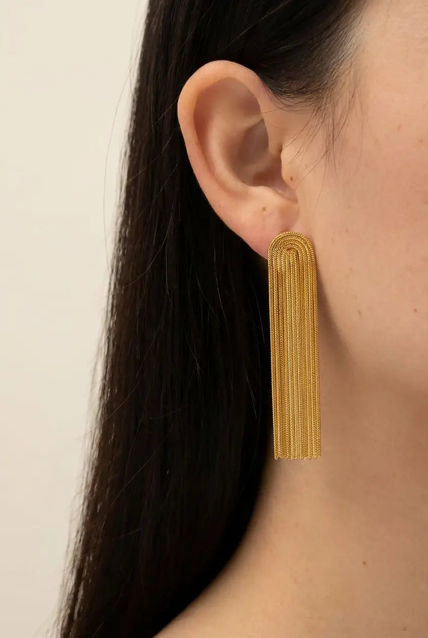 A close-up of a model's ear wearing a single gold statement earring with a textured, ribbed arch design.