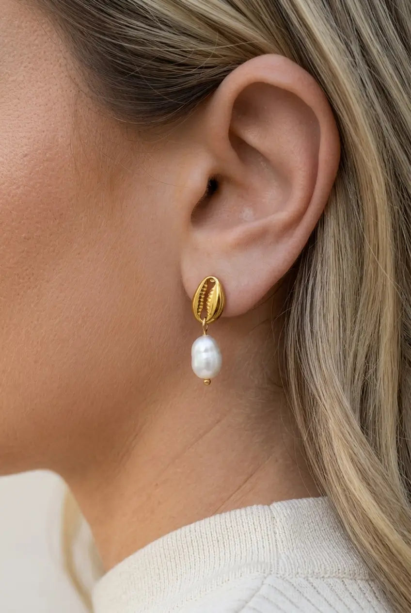 A close-up of a woman's ear wearing a gold ear cuff earring with a dangling white pearl.