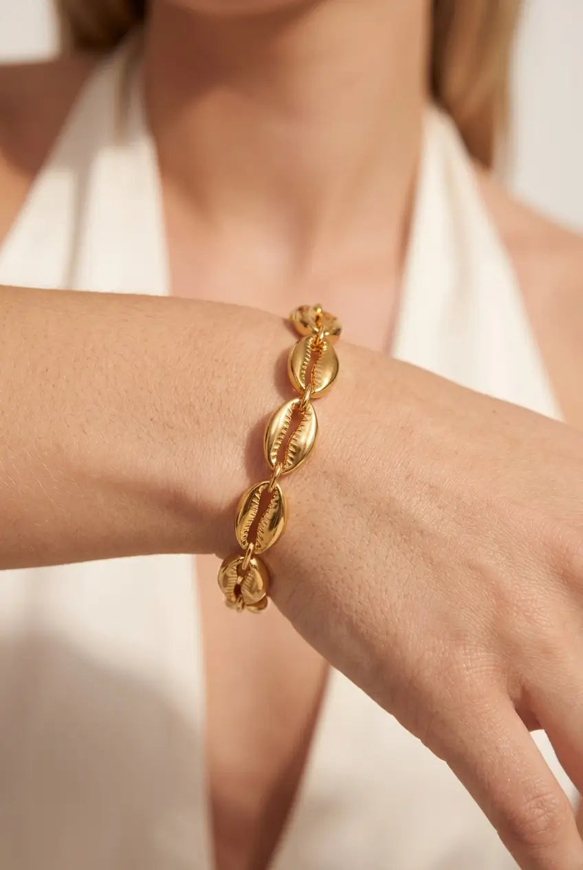 A close-up of a gold chain bracelet made of textured cowrie shells, worn on a person's wrist.