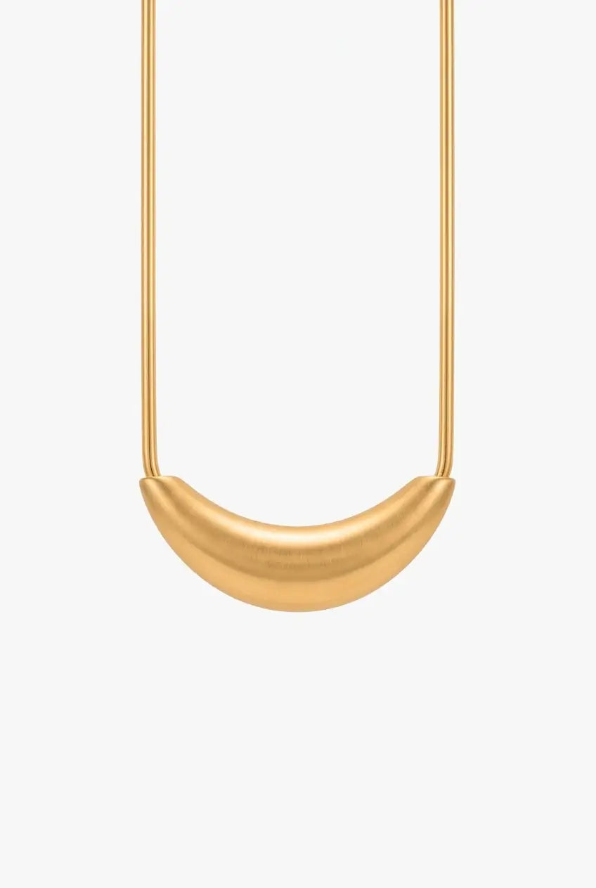A minimalist gold pendant necklace featuring a smooth, curved crescent or half-moon shape suspended from a fine gold chain, set against a solid off-white background.
