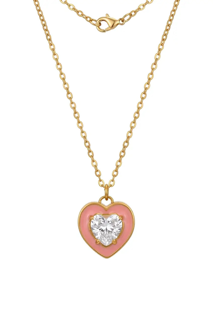 A gold heart pendant necklace with a pink enamel background and a clear heart-shaped gemstone in the center, shown on a white background.