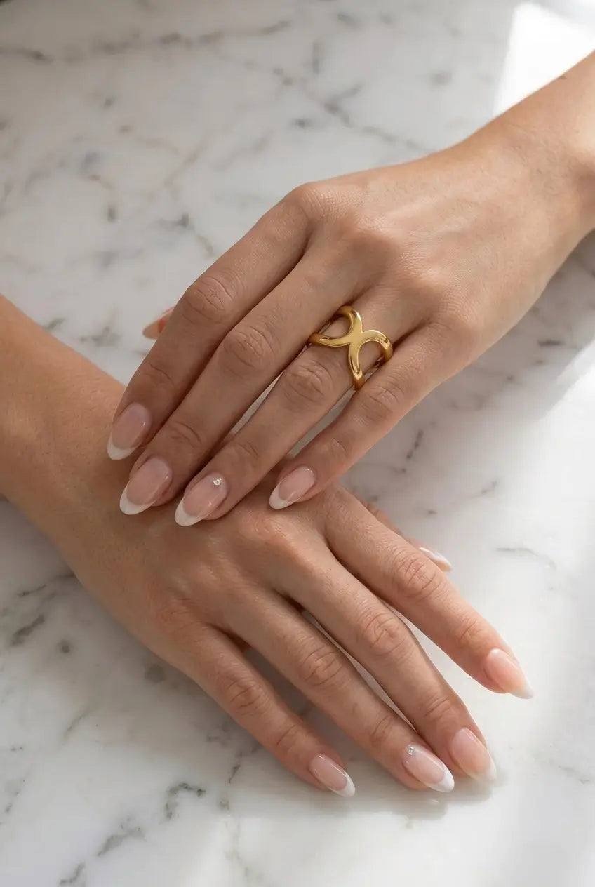 A close-up of two hands resting on a white marble surface, with the right hand wearing a gold ring featuring an abstract, intertwined loop design.