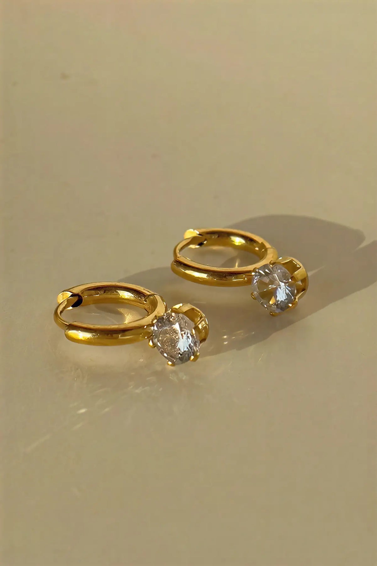 Solitaire crystal huggie hoops flat lay — YUBAMA 18K gold PVD crystal drop earrings