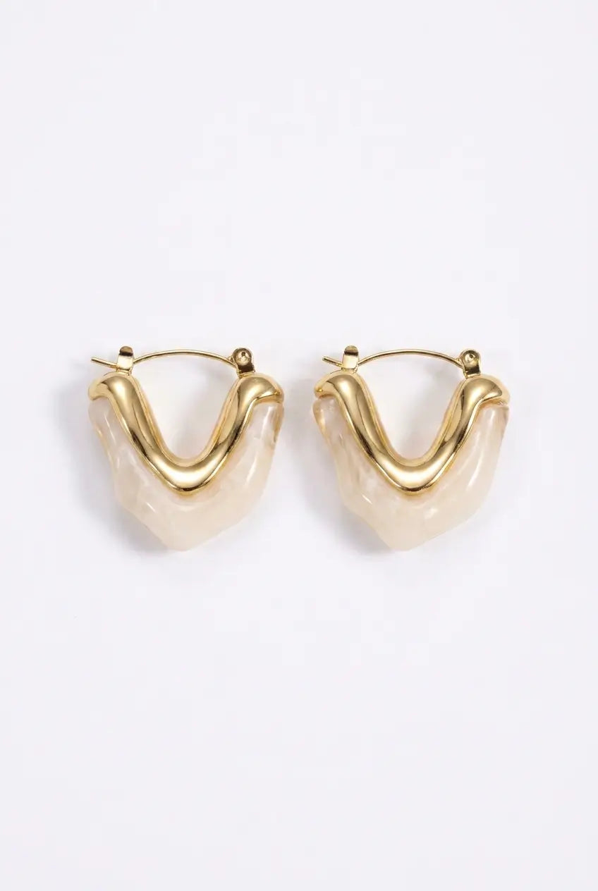 A pair of gold-tone hoop earrings with a wavy, organic curved design and a milky translucent cream resin center, shown on a plain white background.