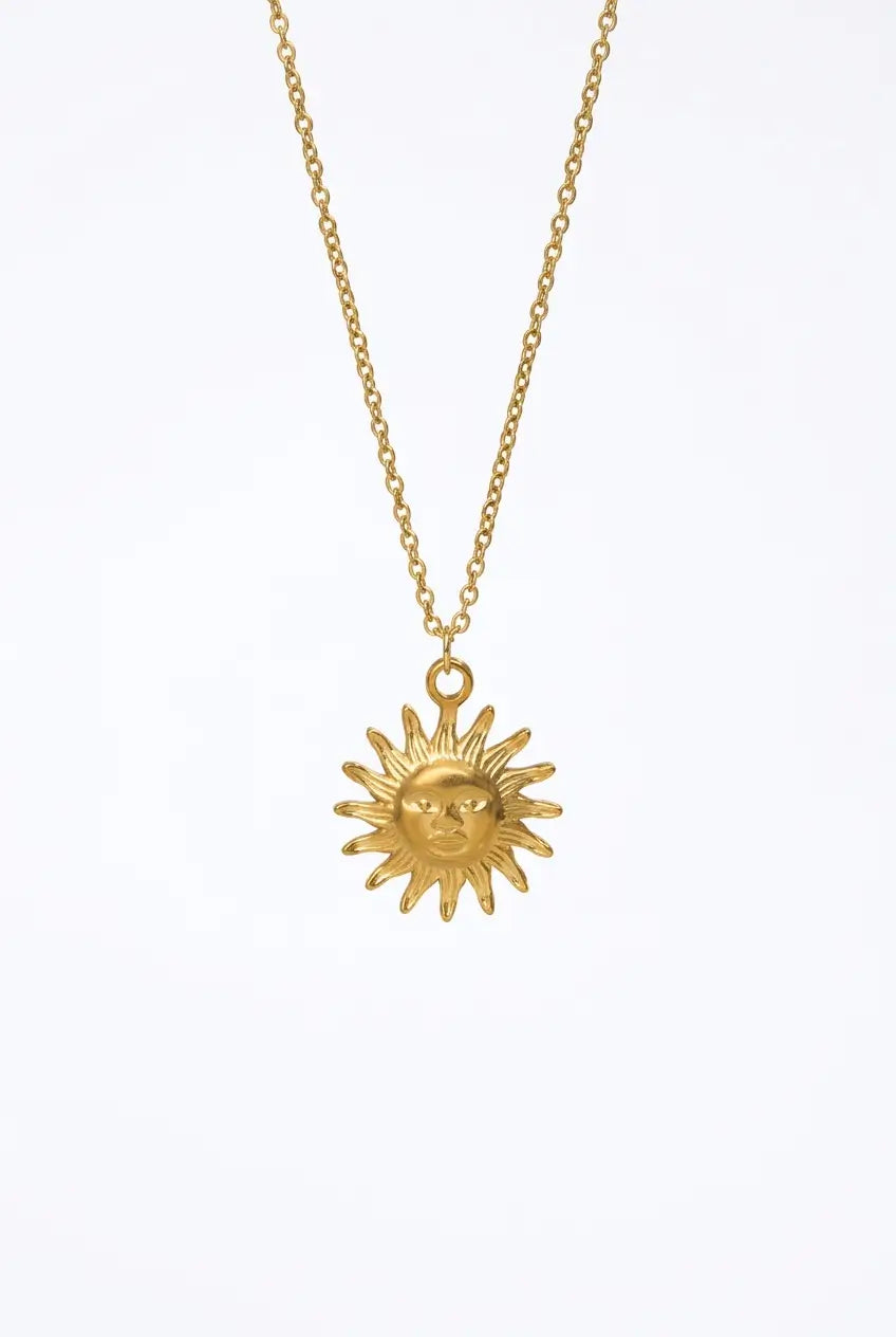 A gold sun pendant necklace with a detailed sun face and rays, hanging from a delicate gold chain against a plain white background.