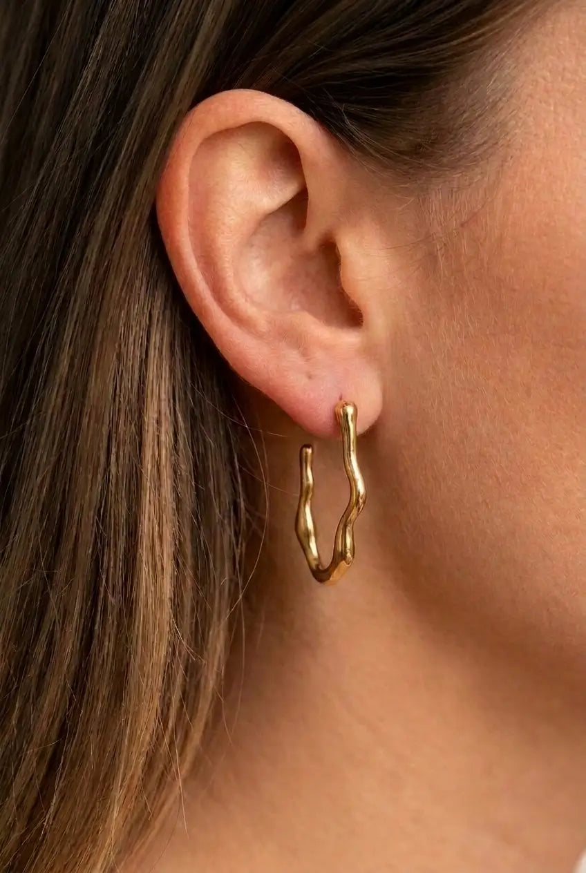 A close-up of a model's ear wearing a polished gold wavy hoop earring.
Details
