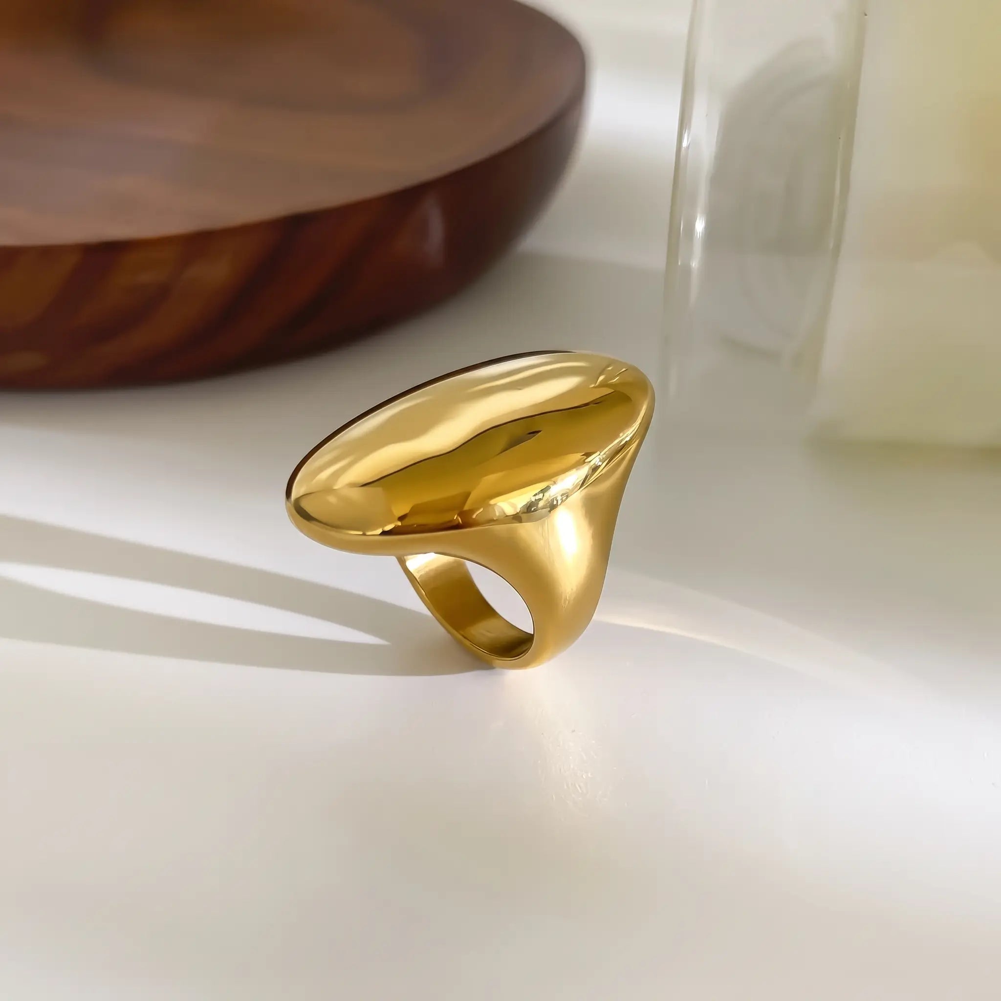 A chunky, oversized gold ring with a smooth, organic, rounded shape, resting on a white surface with soft shadows.