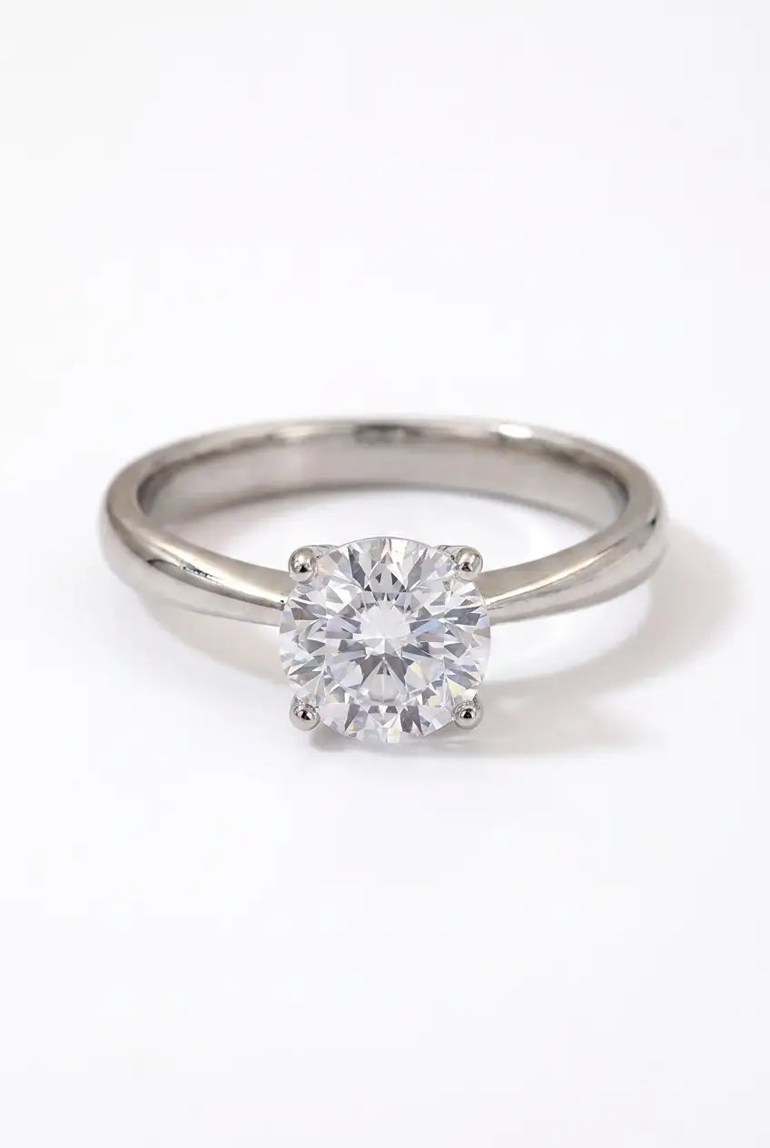 A classic solitaire engagement ring featuring a round brilliant-cut diamond set in a polished silver-colored metal band, shown on a clean white background.