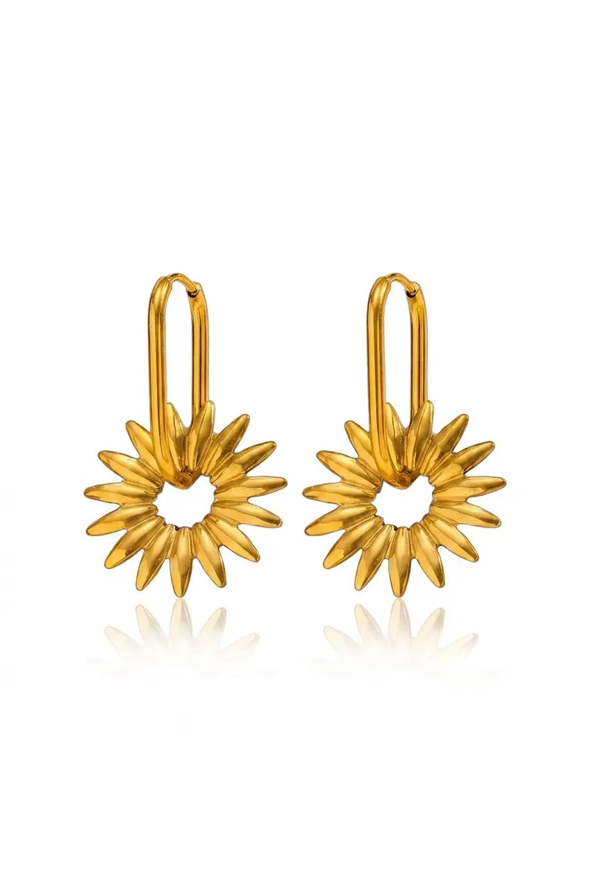 A pair of gold daisy drop earrings with textured petals and a central open circle, hanging from simple gold ear loops on a white background with a soft reflection.