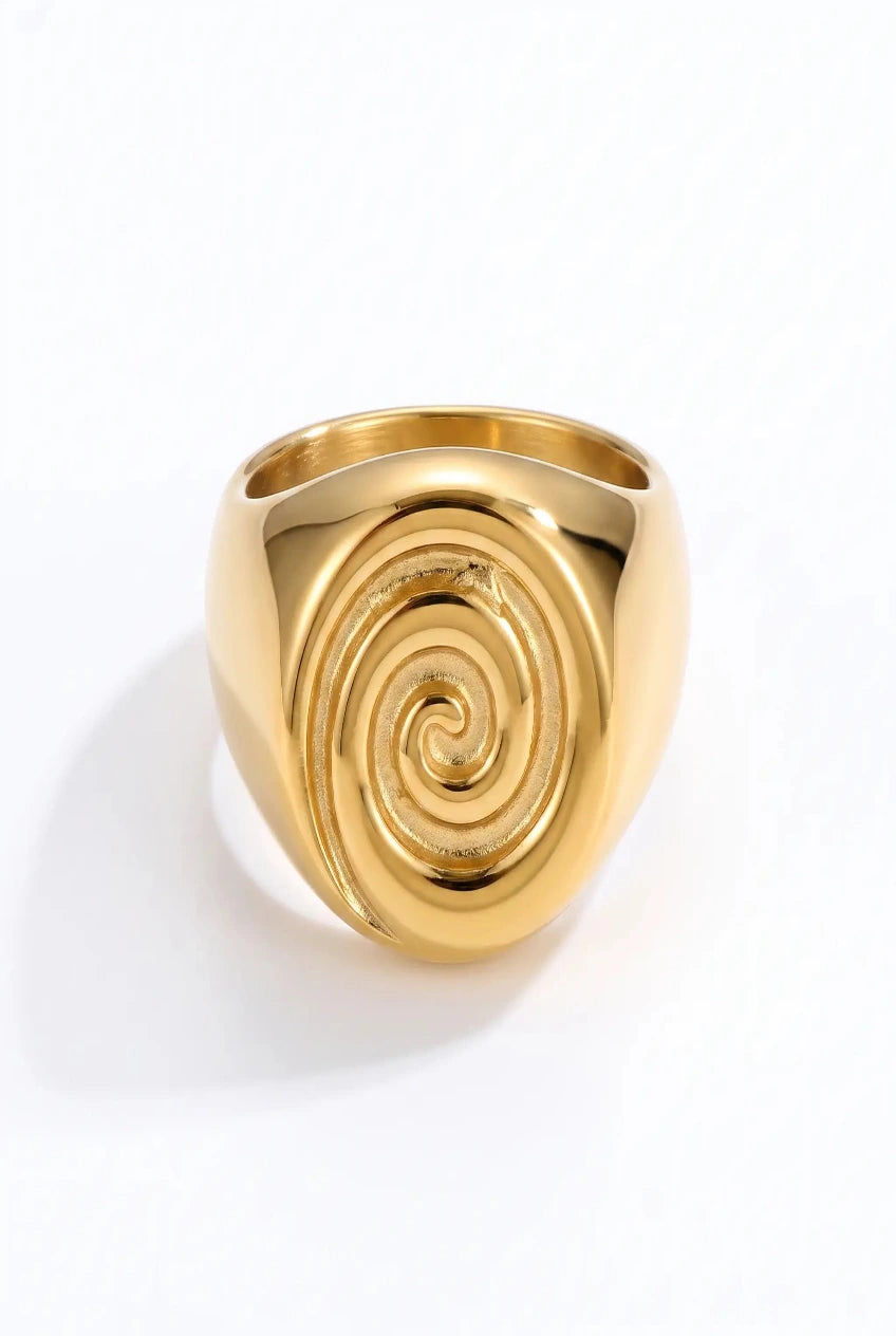 A polished gold signet-style ring with a raised spiral design on the face, photographed on a clean white background.