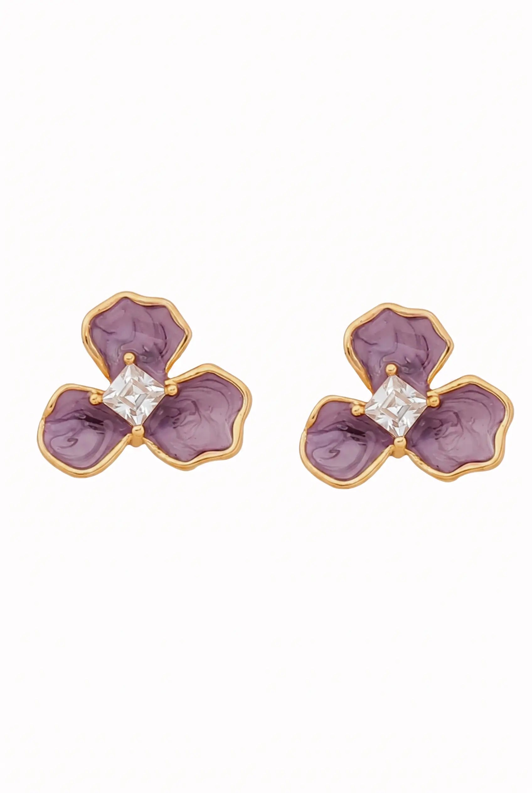 A pair of gold flower-shaped stud earrings with purple enamel petals and a clear square-cut center stone, shown on a plain white background.