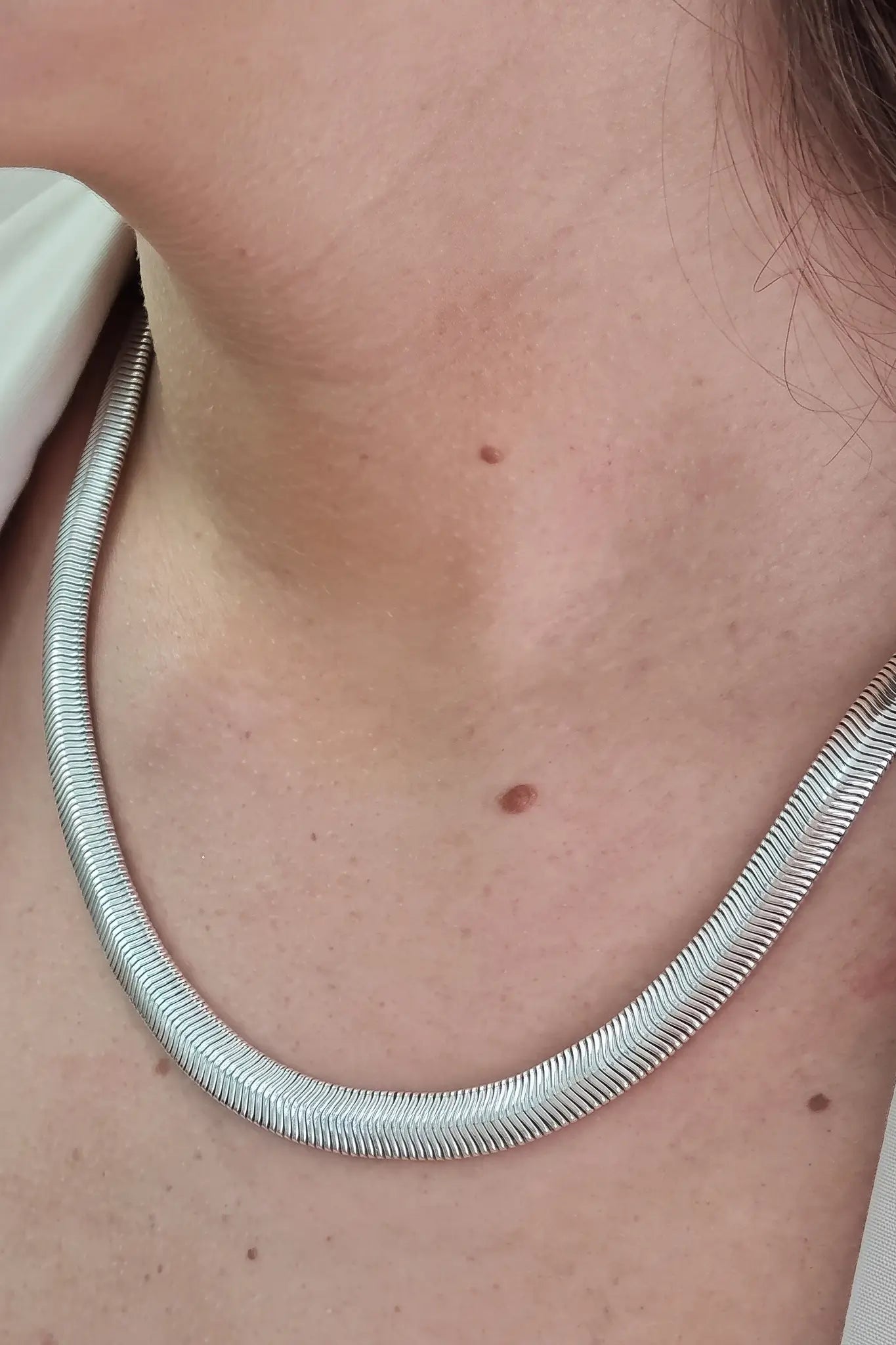 A close-up of a person's neck and upper chest wearing a silver snake chain necklace.