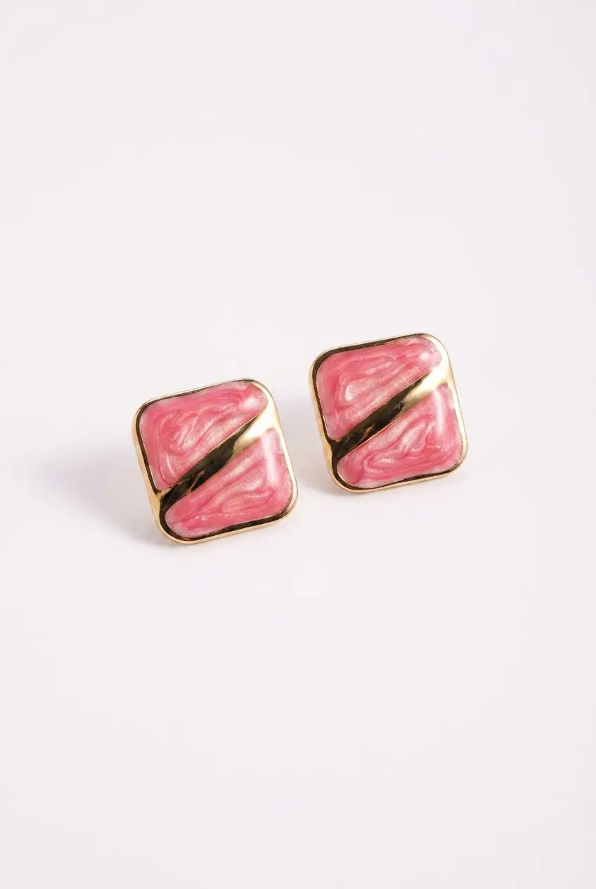 A pair of square stud earrings with a pink and white marble pattern, divided diagonally by a metallic gold stripe, set in gold-tone metal on a light gray background.