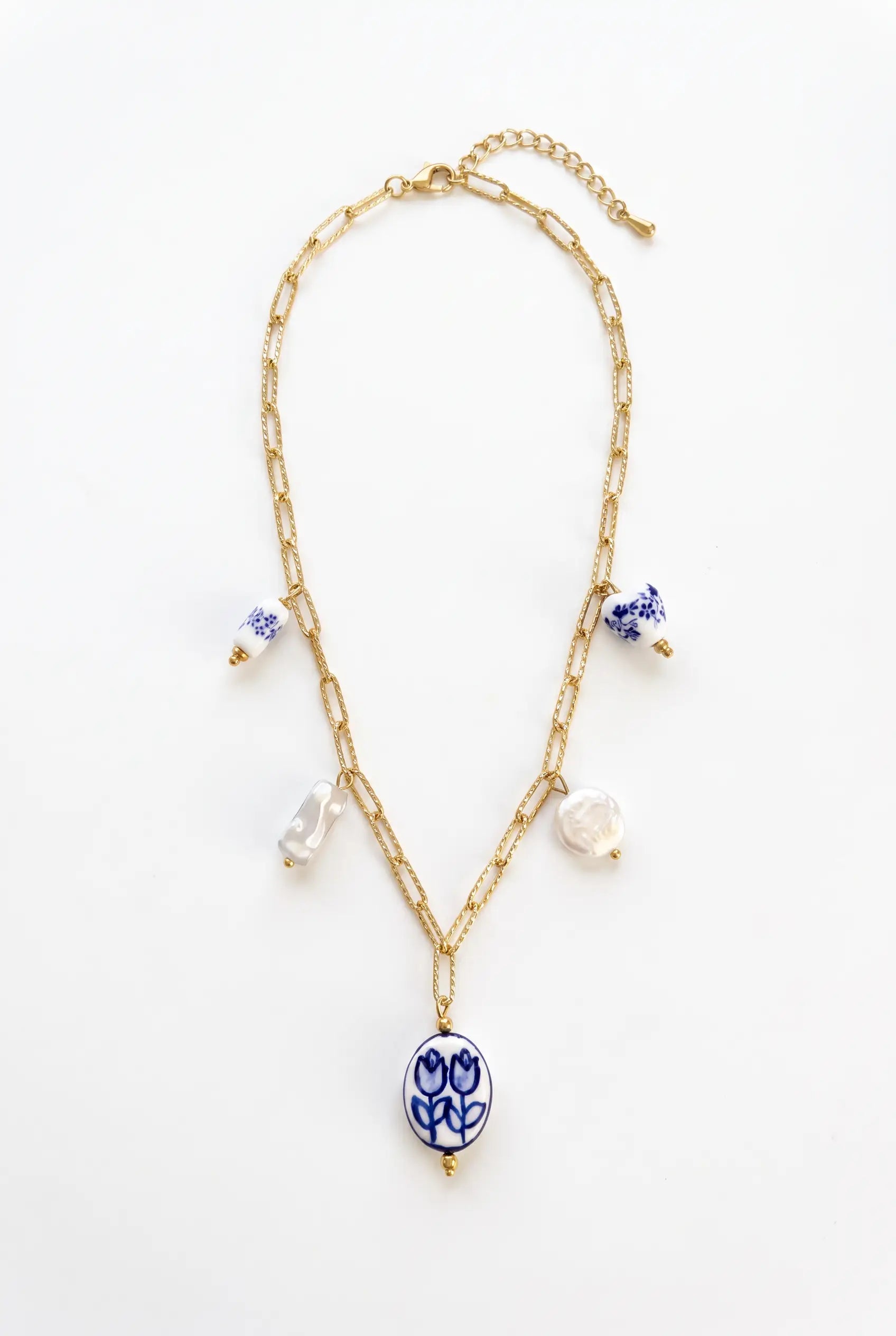 A gold chain necklace featuring a central oval pendant with a blue floral pattern, accented by small white pearl-like beads and blue-and-white ceramic charms, displayed on a clean white background.
